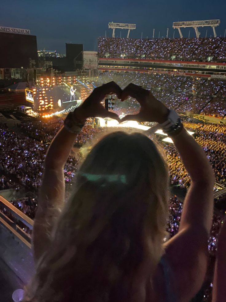 a woman making a heart shape with her hands at a concert in front of an audience