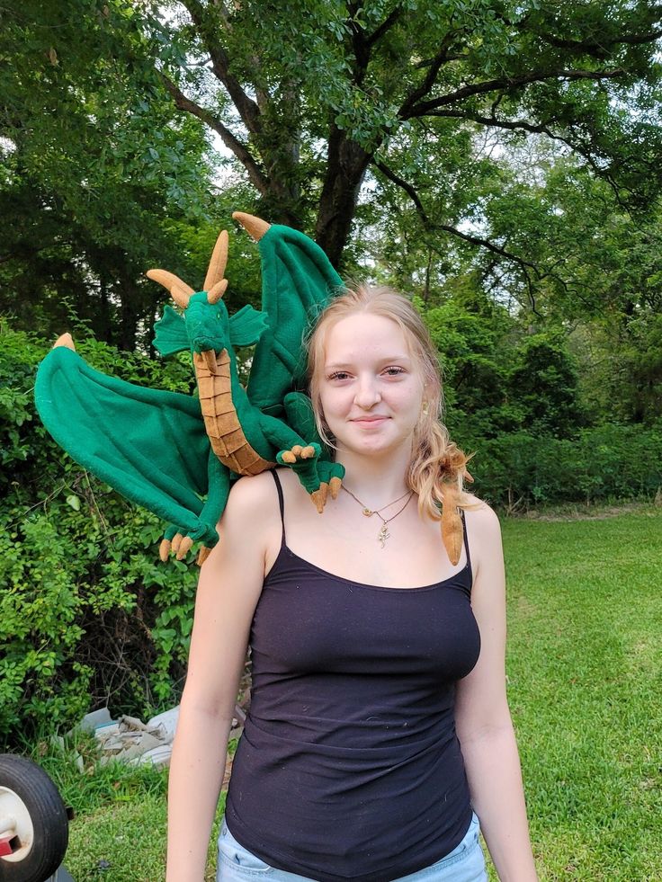 a girl standing in the grass with a green dragon costume on her head