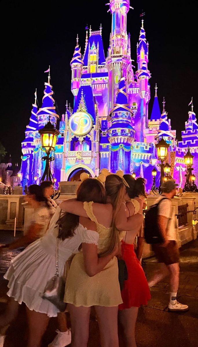 two girls hugging each other in front of a castle at night with lights on it