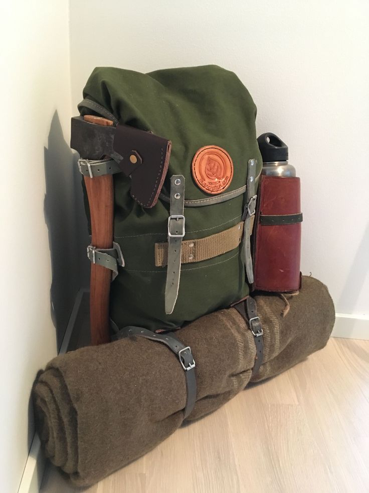 a green backpack sitting on top of a wooden floor next to a pair of boots