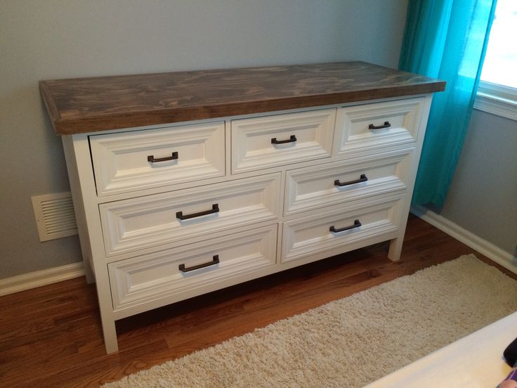 a white dresser with wooden top and drawers in a room next to a blue curtain