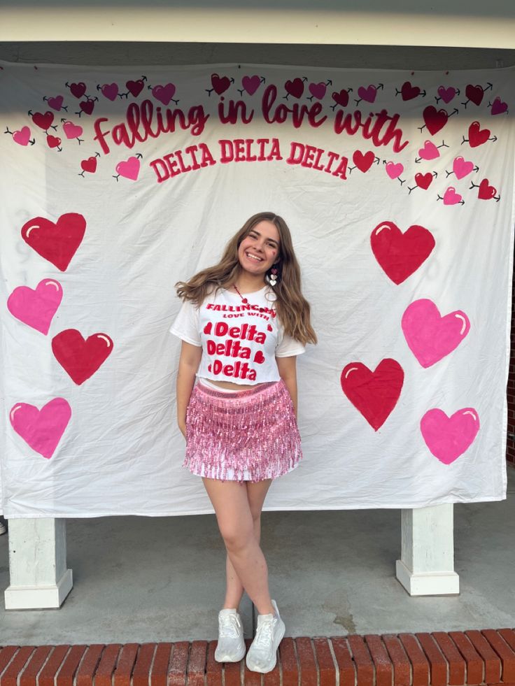 a girl standing in front of a banner with hearts on it that says falling in love with delta delta delta