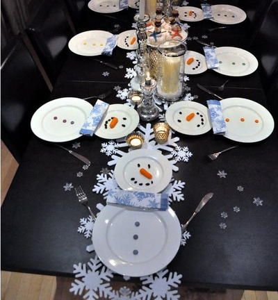 the table is set with plates, silverware and snowflakes on black paper