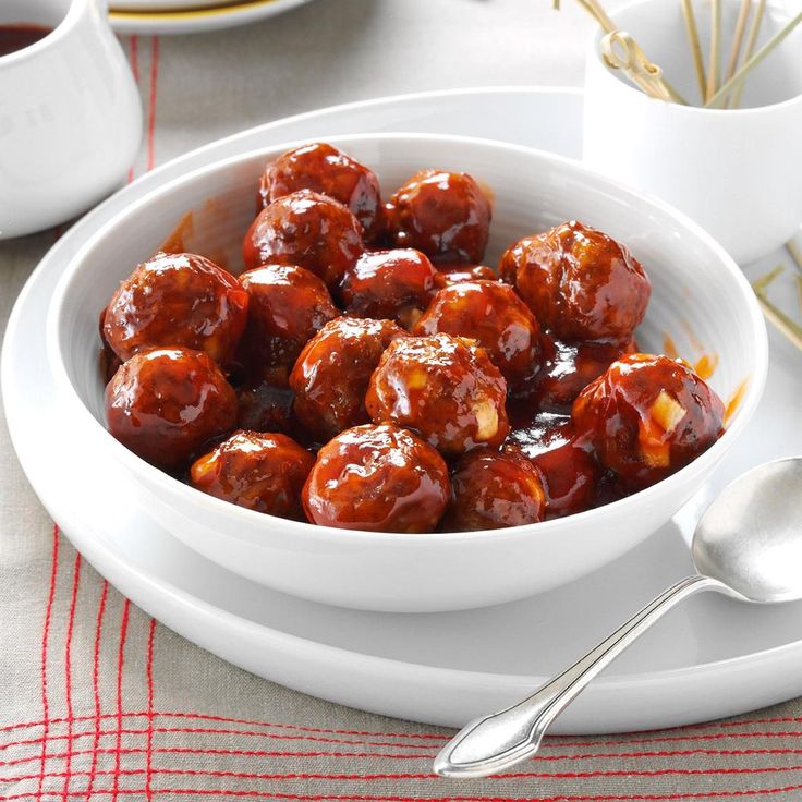 a bowl filled with meatballs sitting on top of a table next to cups and spoons