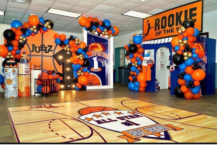 an indoor basketball court decorated with orange, black and blue balloons in the shape of hoops