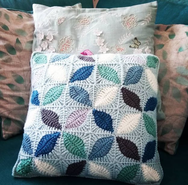 a crocheted pillow sitting on top of a green couch next to two pillows