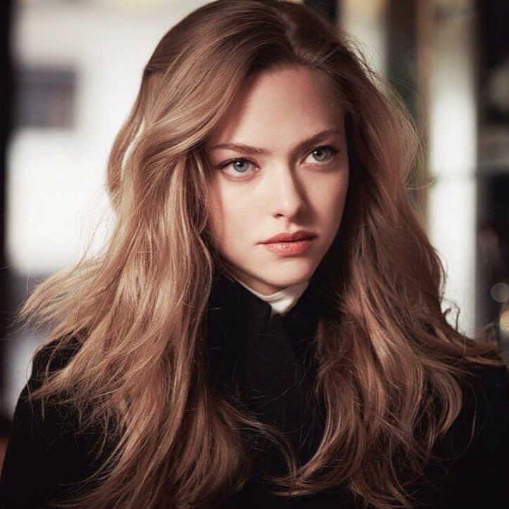 a woman with long hair and blue eyes looks into the camera while wearing a black coat