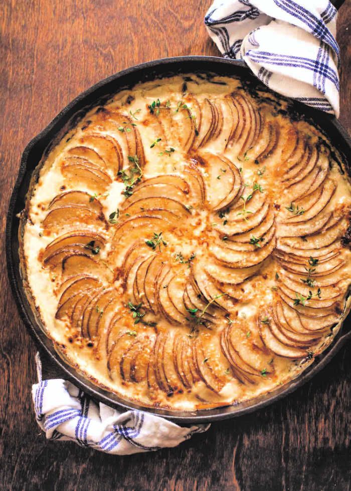 baked potato casserole in a cast iron skillet on a wooden table with a blue and white checkered napkin