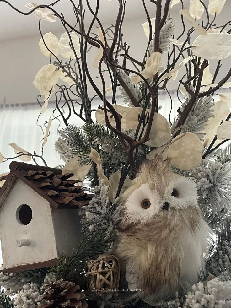 an owl is sitting on top of a christmas tree with white flowers and pine cones