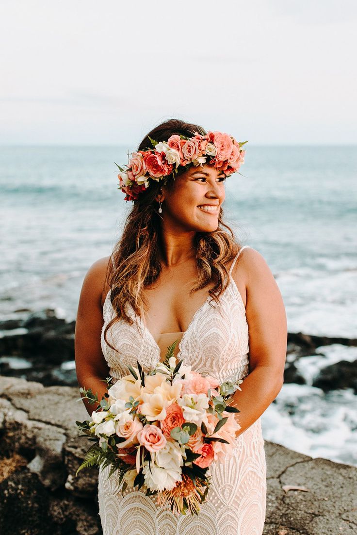 a woman standing on top of a rocky beach next to the ocean wearing a flower crown