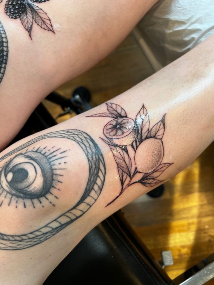 two people with tattoos on their legs, one has an eye and the other has flowers