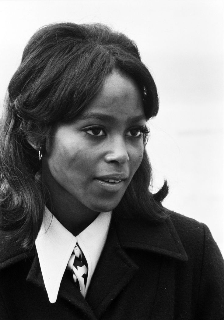 a black and white photo of a woman wearing a coat, tie and dress shirt