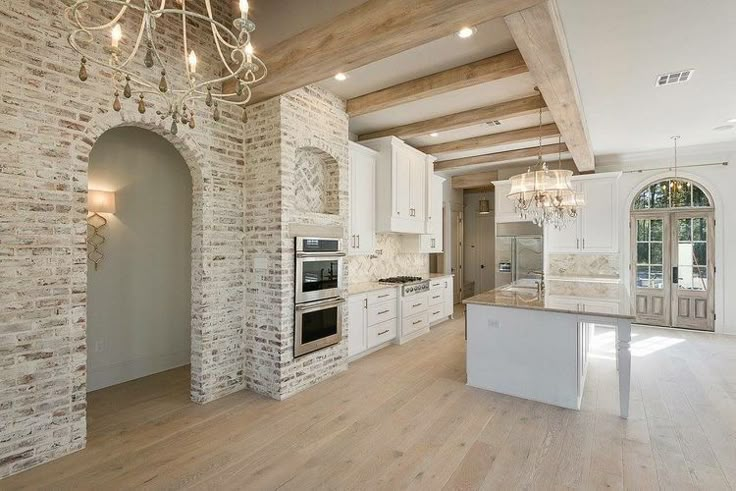 a large kitchen with white cabinets and an island in front of a brick wall that has a chandelier hanging from it's ceiling