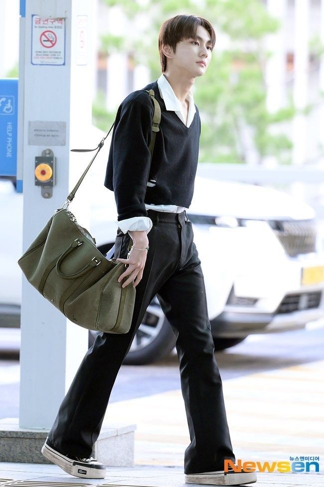 a man walking down the street carrying a green handbag in his right hand and wearing black pants