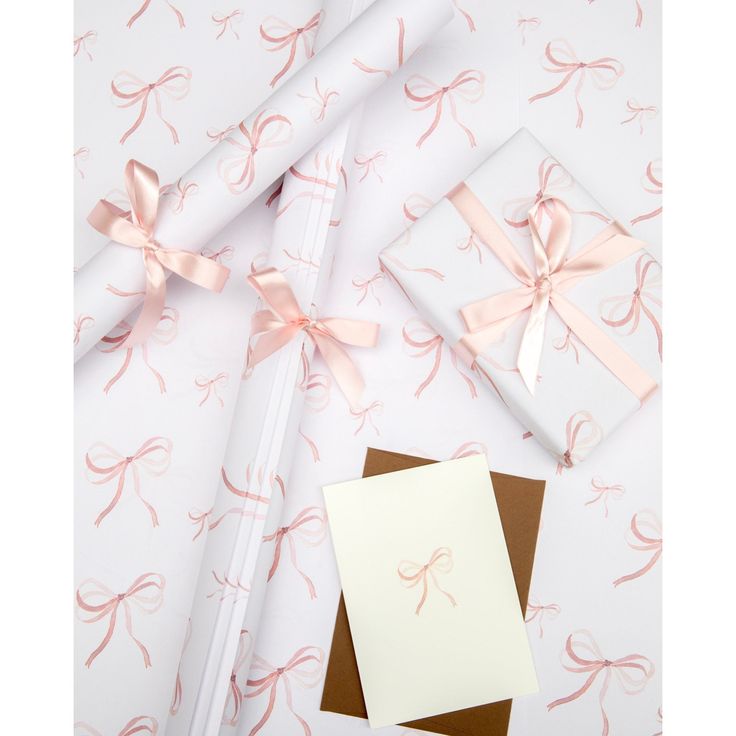 three wrapped presents with pink bows on them next to a notepad and envelopes