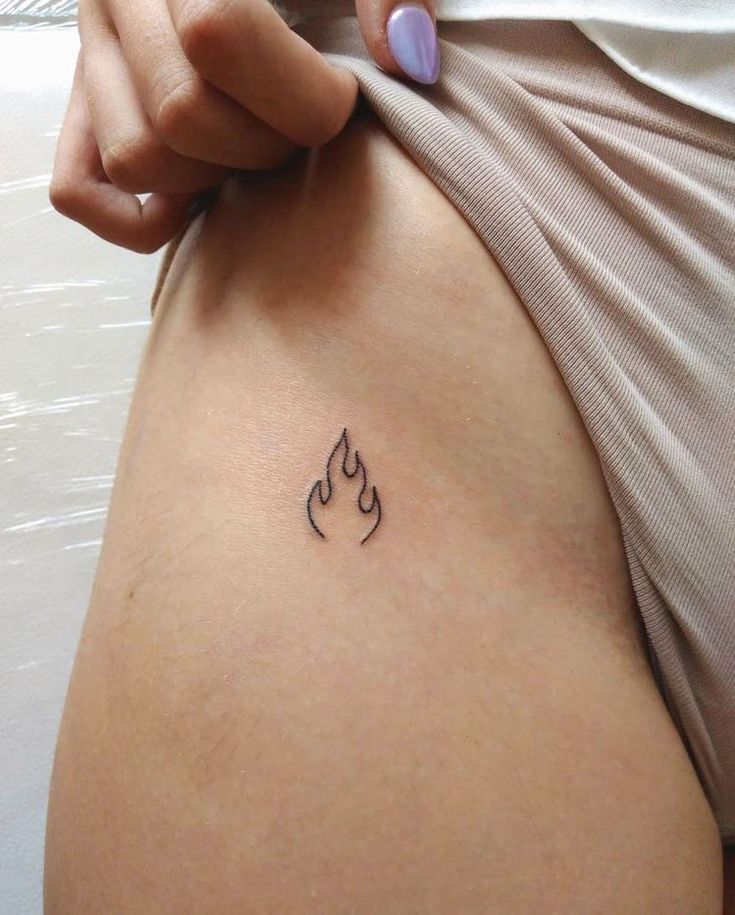 a woman's stomach with a small fire tattoo on her left side ribcage