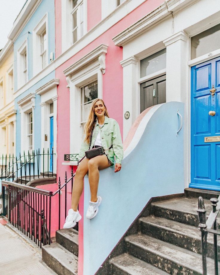 a woman sitting on top of a blue and pink wall next to some stairs in front of colorful buildings