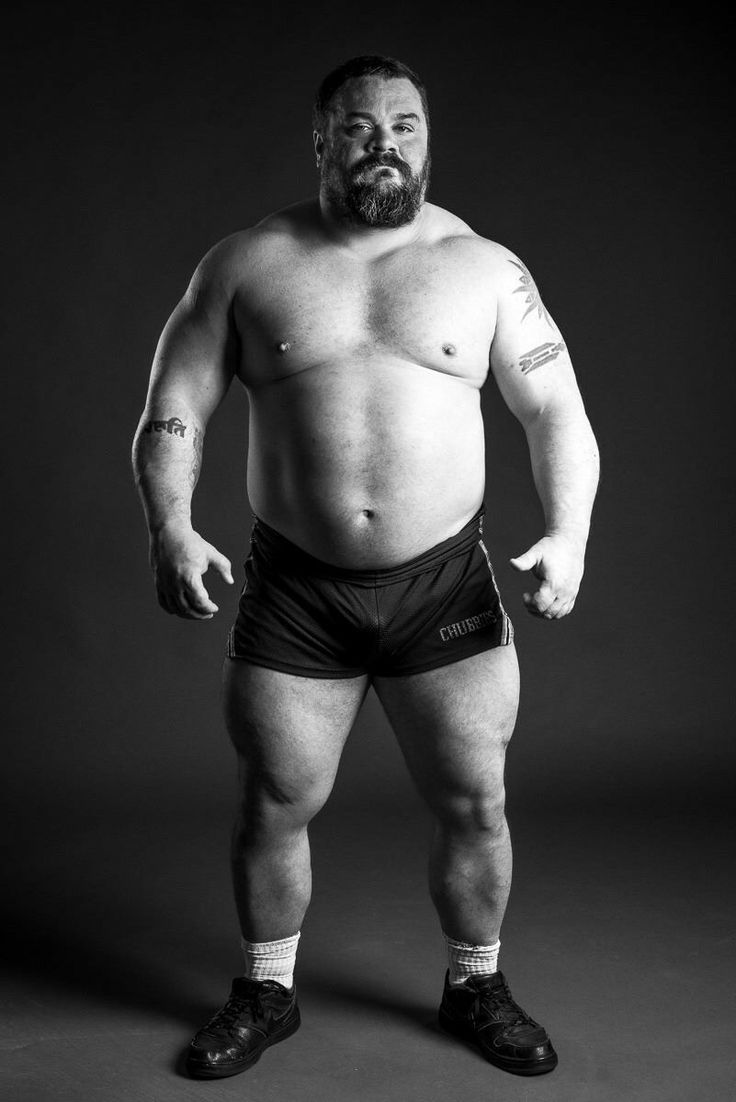 a man with no shirt and black shorts standing in front of a gray background holding his hands on his hips