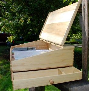 an open wooden box sitting on top of a bench in front of some grass and trees