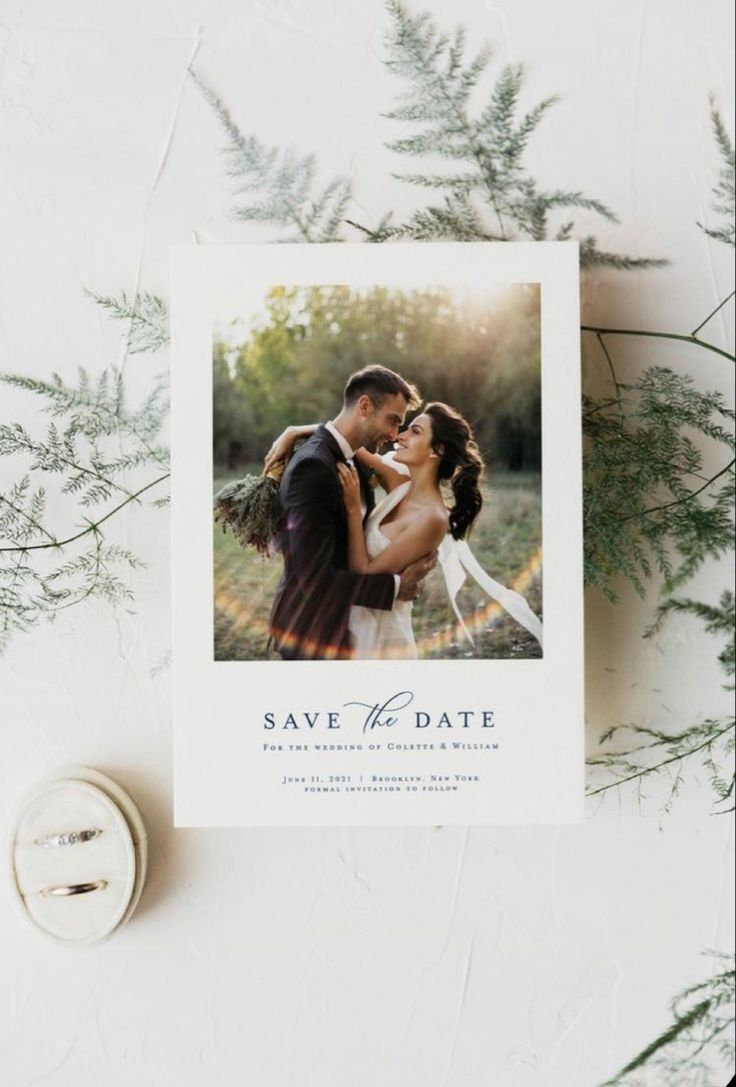 save the date card with an image of a bride and groom kissing in front of greenery