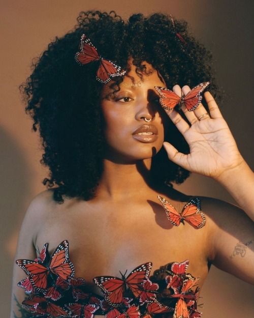 a woman with butterflies on her shoulder and hands in front of her face, posing for the camera