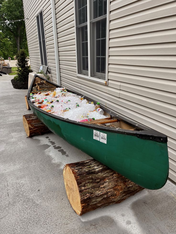 a green canoe sitting on the side of a house next to a log with candy in it