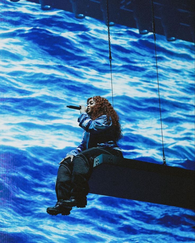 a woman is sitting on the edge of a boat while holding a microphone in her hand