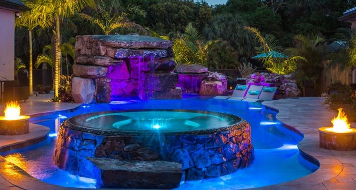 an outdoor hot tub lit up at night with fire lights on the sides and around it