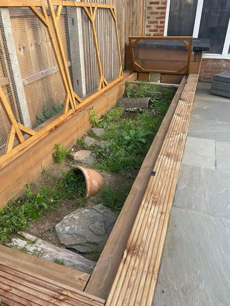 an outdoor area with rocks and grass in the ground next to a wooden fenced off building