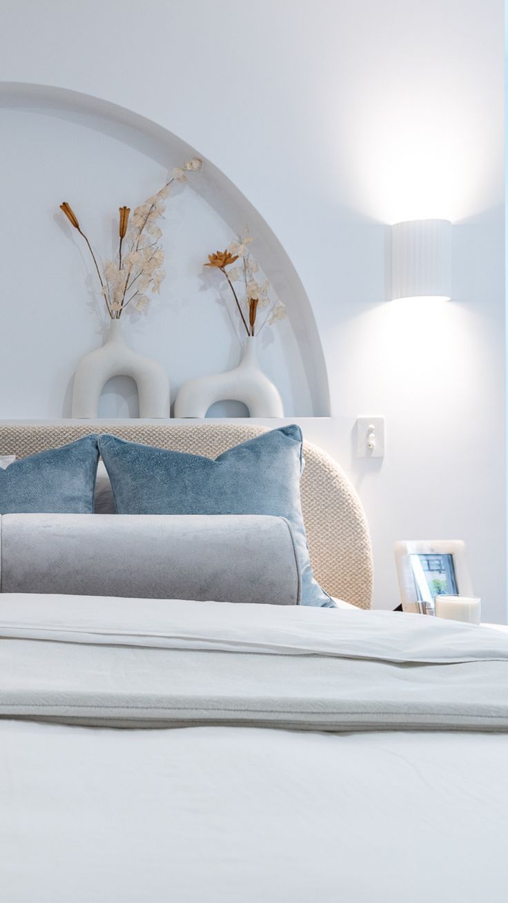 a white bed with two vases on the headboard and pillows in front of it