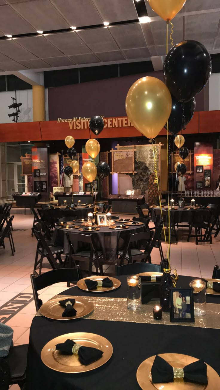 black and gold balloons are hanging from the ceiling at a banquet table set for an event