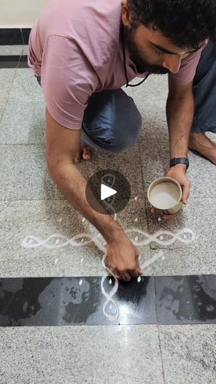 a man kneeling down on the ground while holding a coffee cup and drawing with chalk