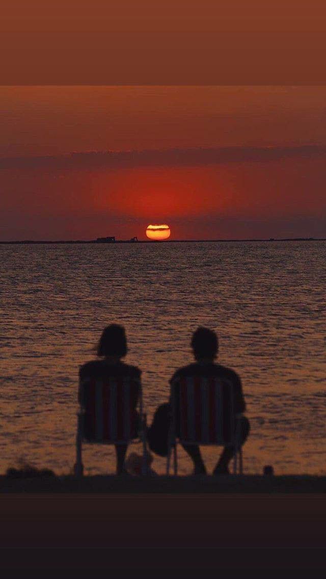 two people sitting in chairs watching the sun go down over the ocean at sunset or sunrise