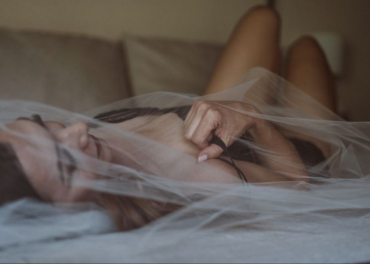 a woman laying on top of a bed covered in white sheets