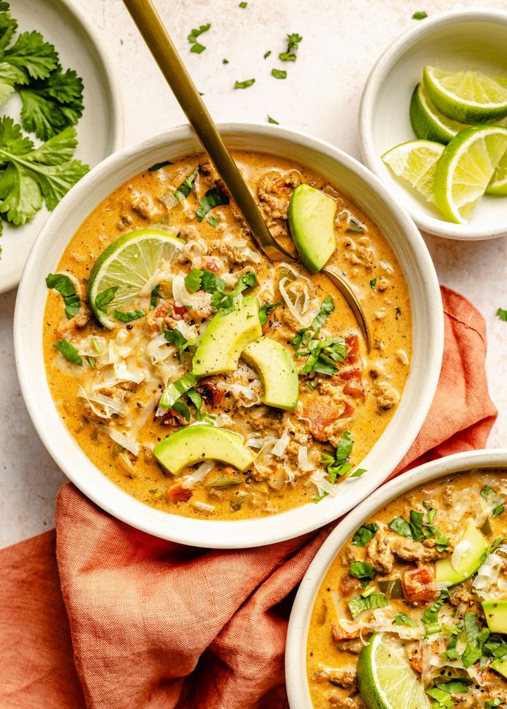 two bowls of soup with limes, cilantro and avocado on the side