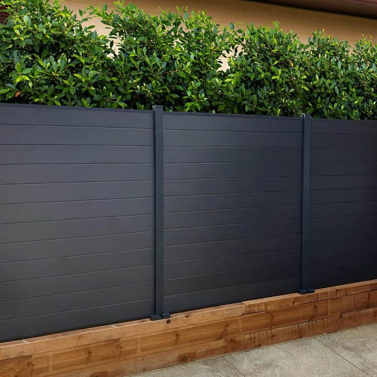 a wooden planter filled with green plants next to a fenced in area on the side of a building