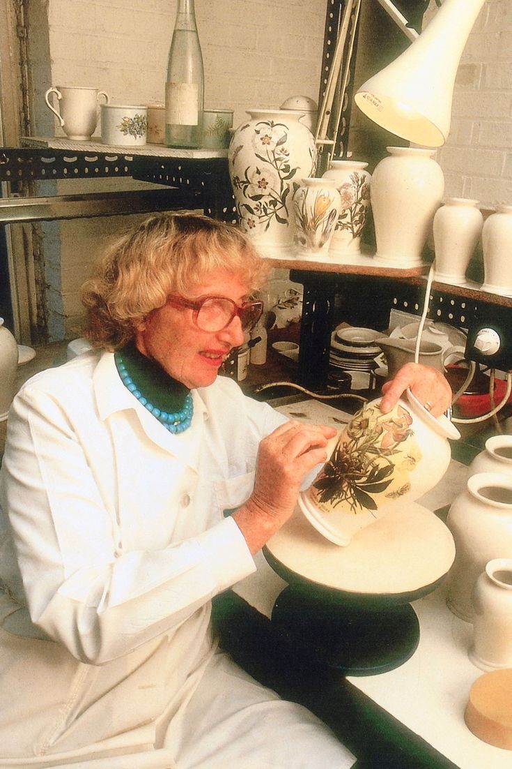 a woman is sitting at a table making vases