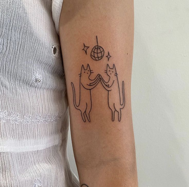 a woman with a cat tattoo on her arm holding a globe and two cats in the middle