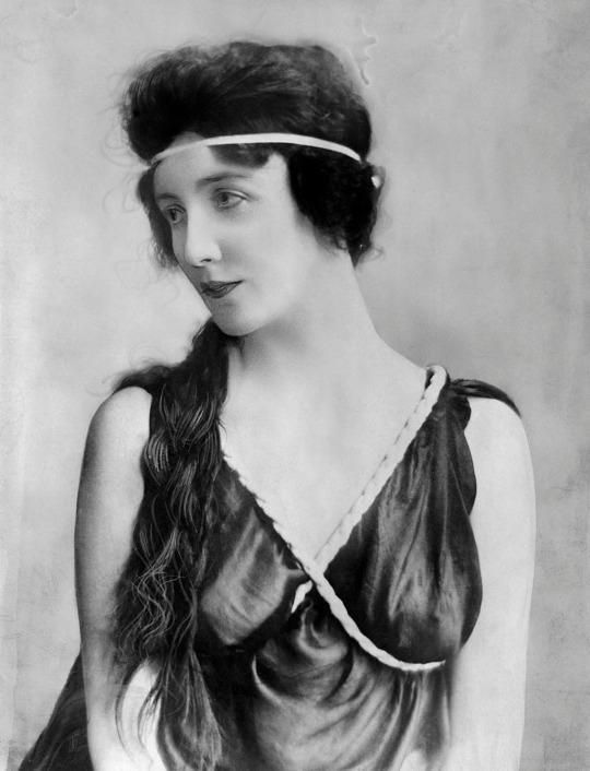 an old black and white photo of a woman with long hair wearing a headband