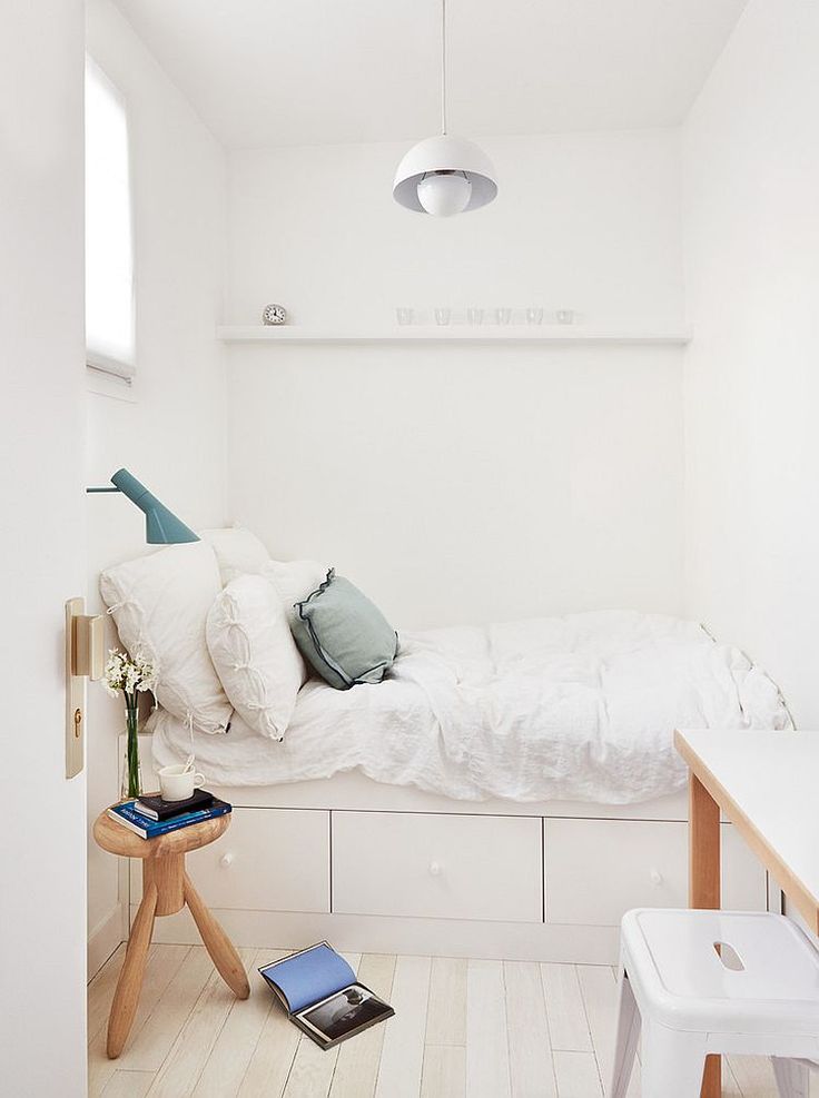 a bedroom with white walls and flooring has a small bed on one side, an end table on the other