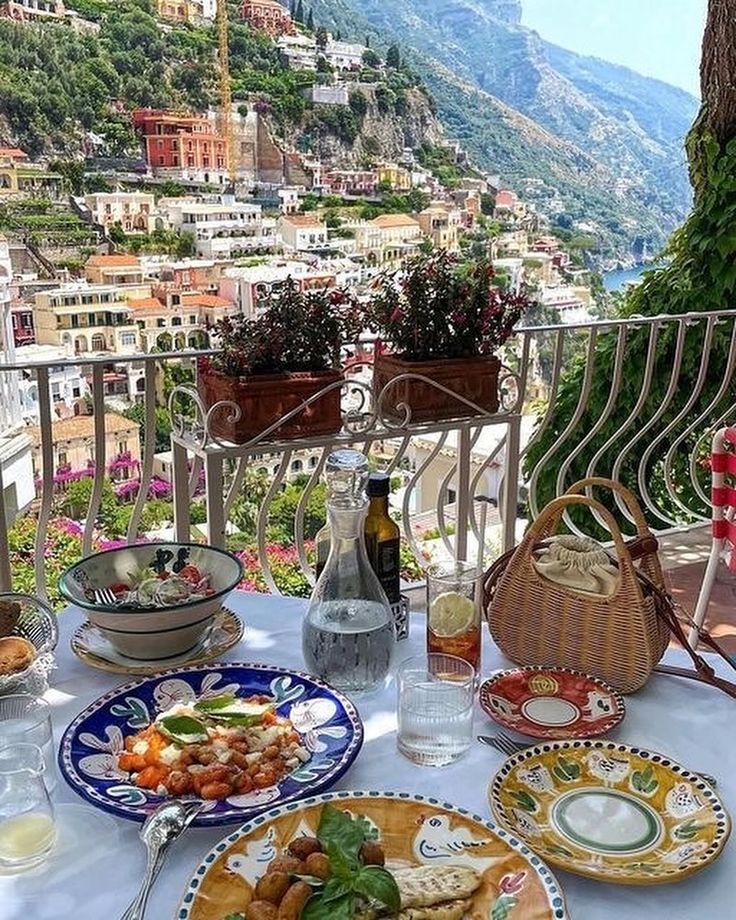 a table topped with plates and food on top of a balcony next to a mountain