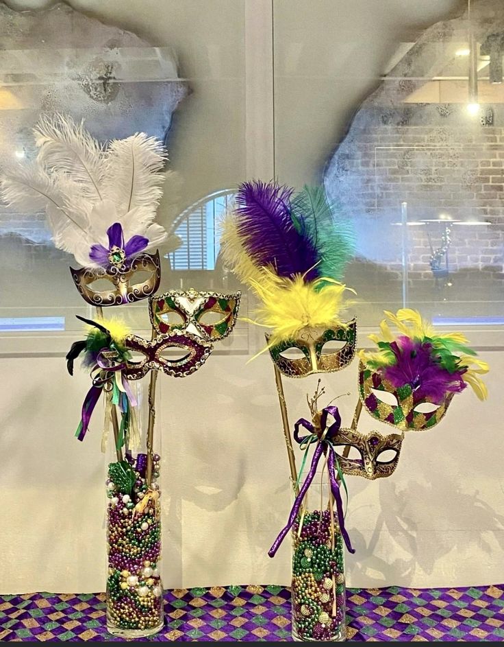 two tall vases with masks and feathers in them sitting on a purple table cloth