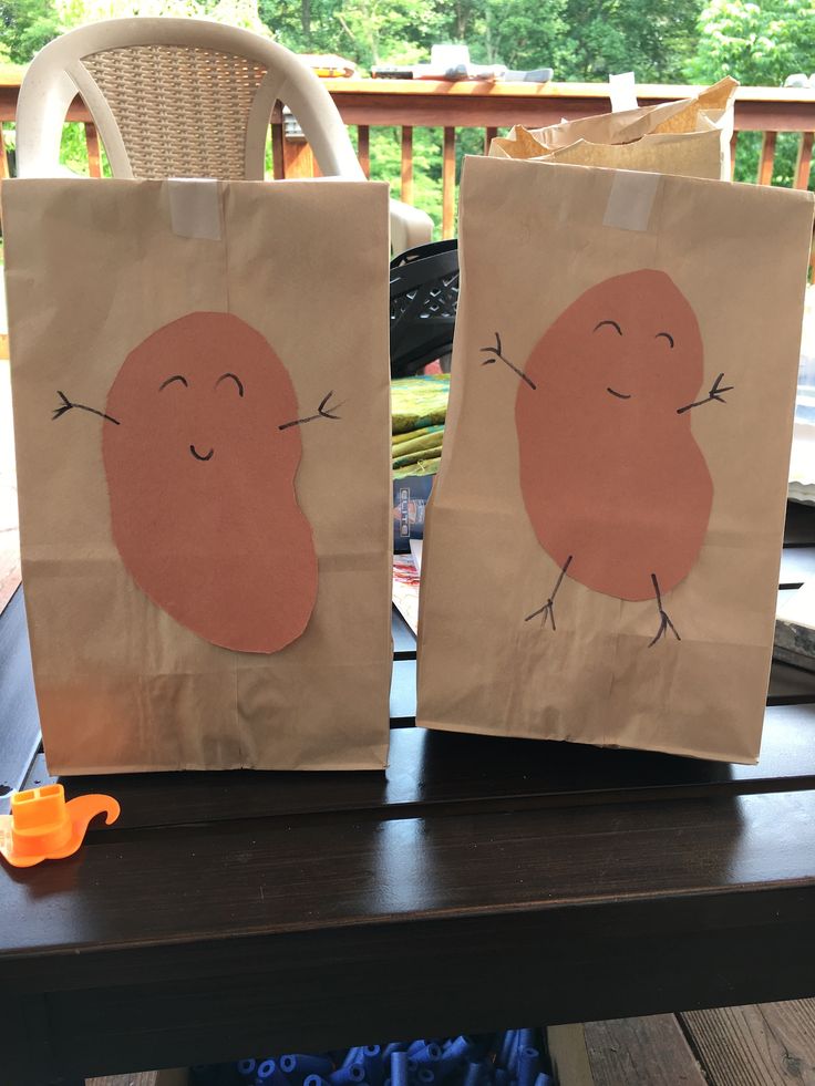 two brown bags with faces on them sitting on a table next to an orange object