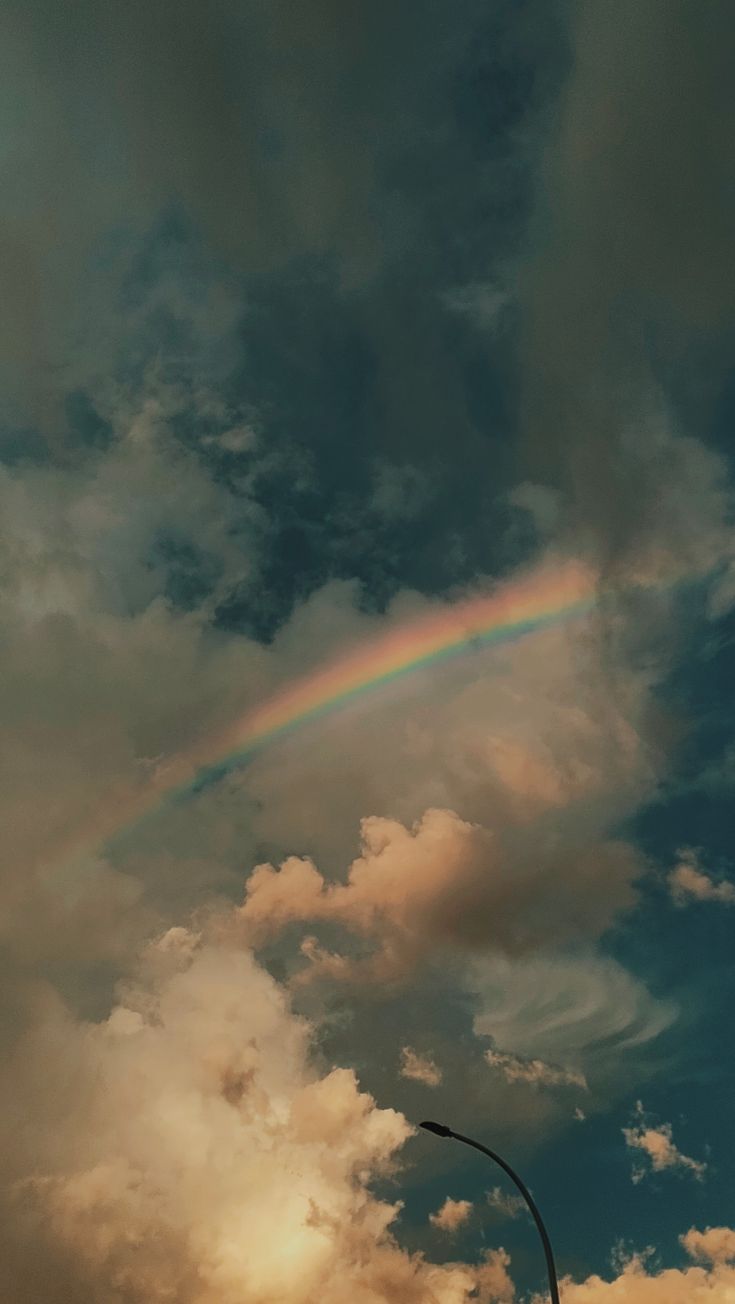 a rainbow is seen in the sky over a street light and some clouds above it