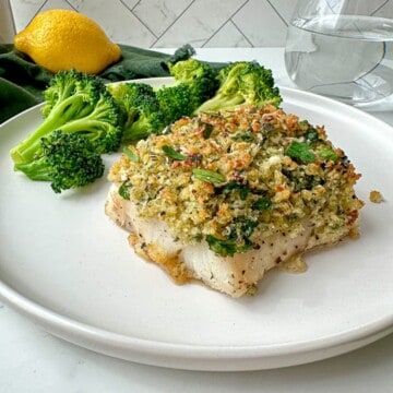 a white plate topped with fish and broccoli on top of a kitchen counter