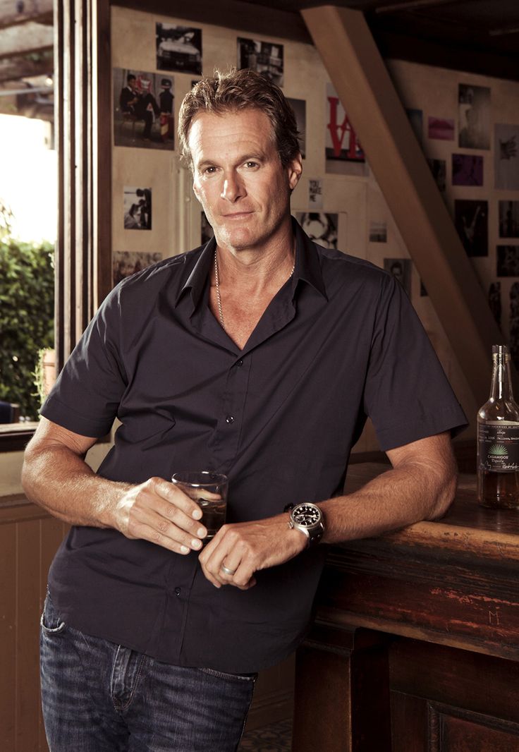 a man standing in front of a bar holding a wine glass and looking at the camera