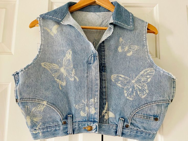 Beautiful light washed denim zipper vest. This is a DIY design made from a pair of Upcycled Wrangler jeans. #denimvest #recycleddenim #upcycleddenim #recycledfashion #butterflies #Stenciledenim #Denimclothes #denimstyle #denimfashion Summer Acid Wash Denim Jacket, Spring Acid Wash Denim Vest, Casual Denim Vest For Festivals, Casual Denim Festival Vest, Casual Upcycled Denim Vest For Spring, Summer Festival Medium Wash Denim Vest, Casual Upcycled Sleeveless Denim Vest, Beachy Accessories, Saint Simons Island