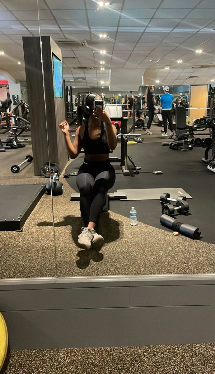 a woman is taking a selfie in the gym with her phone up to her ear