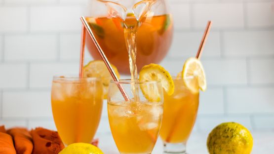 two glasses filled with orange juice and lemons next to some other fruit on the table