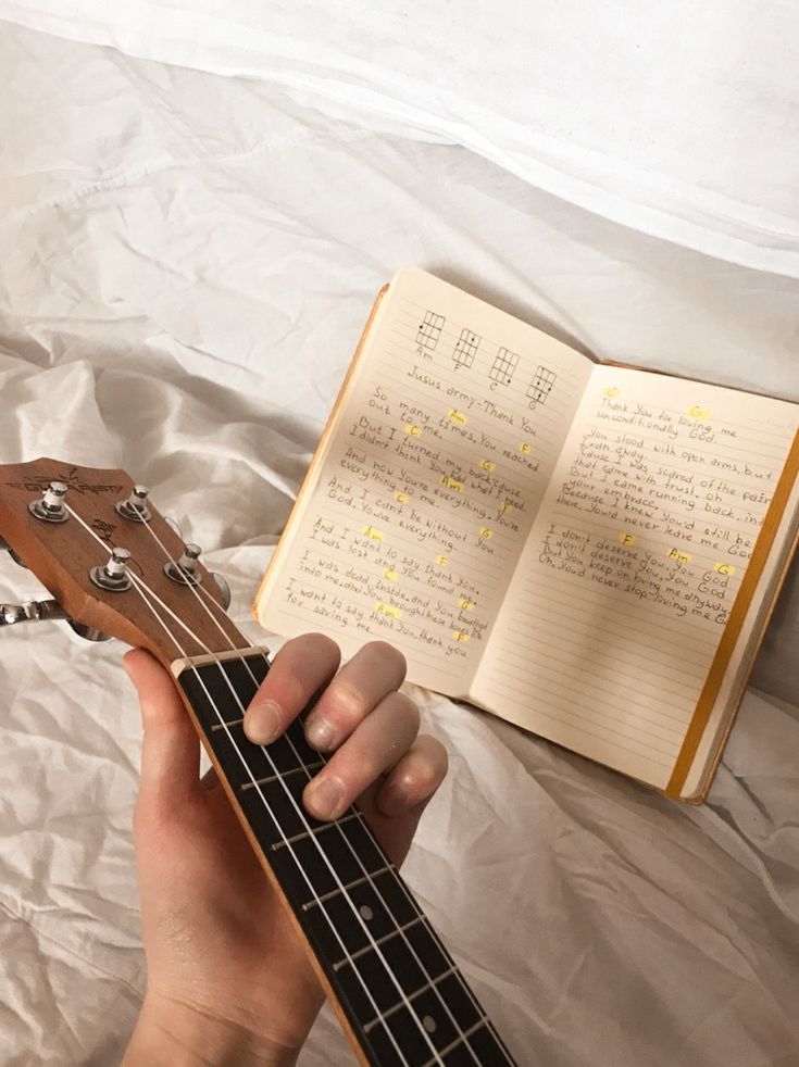 a person is holding an ukulele in their hand and reading it on the bed